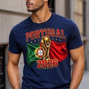 May include: Navy blue t-shirt featuring the word "PORTUGAL" in red and gold lettering, with a gold trophy and the year "2026". The design includes the Portuguese flag and a red flag.