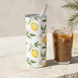 Puede incluir: Un vaso blanco con un estampado de lim&oacute;n y hojas, una pajita plateada y un vaso transparente de caf&eacute; helado. El vaso tiene una tapa plateada y est&aacute; decorado con limones amarillos y hojas verdes.