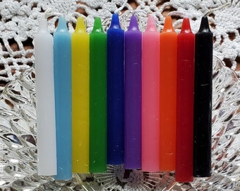 May include: A set of 10 small candles in various colors, including white, yellow, green, blue, purple, pink, orange, red, and black. The candles are arranged in a row on a clear glass plate.