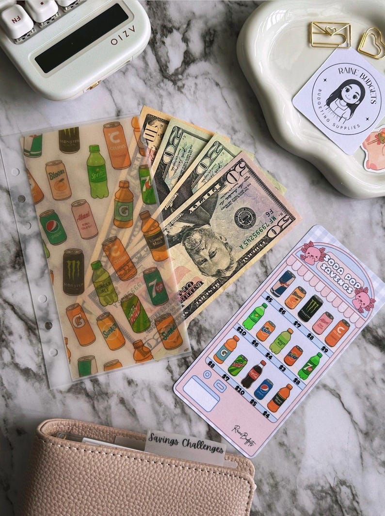Op de afbeelding: Een doorzichtige plastic envelop met een frisdrankontwerp, bankbiljetten en een spaartrackerkaart. De kaart heeft een frisdrankthema met prijzen. Een beige portemonnee met de tekst "Savings Challenges" is ook zichtbaar.