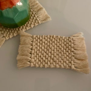 Peut inclure: Deux dessous-de-verre en coton tissé beige avec des franges. Les dessous-de-verre sont faits d'une corde de coton épaisse et texturée et ont un aspect naturel et rustique.