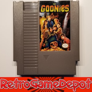May include: A gray Nintendo Entertainment System (NES) game cartridge for "The Goonies." The label features a movie poster-style image of the film's cast. The cartridge has a textured surface and is in good condition.