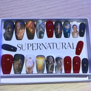 May include: A collection of press-on nails with images of characters from the TV series "Supernatural." The nails are in various colours, including red, black, and those with character portraits. The word "SUPERNATURAL" is printed on the box.