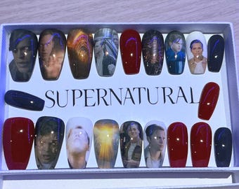 May include: A set of press-on nails featuring images of characters from the television show "Supernatural." The nails are in various colors, including red, black, and those with character portraits. The word "SUPERNATURAL" is printed on the box.