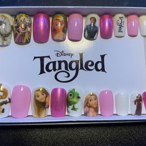 May include: A set of pink and white press-on nails featuring Disney's Tangled characters and the word "Tangled" printed on them.