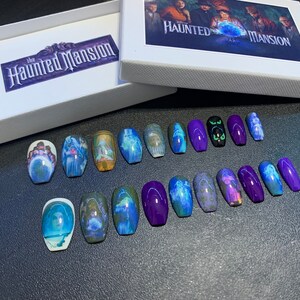 May include: A set of 14 coffin-shaped false nails with a Haunted Mansion theme. The nails feature images of characters and scenes from the Disney attraction, including the Ghost Host, Constance Hatchaway, and the mansion itself. Some nails are solid purple, while others have a clear base with the images printed on them.
