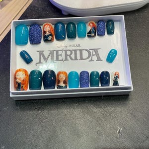 May include: A set of press-on nails featuring a variety of designs. Some nails are solid teal, others are glittery blue, and some feature a cartoon image of Merida from the Disney Pixar movie. The word "MERIDA" is printed on the box.