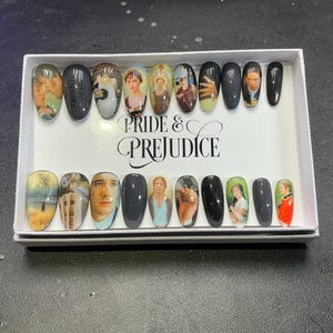 Pode incluir: Um conjunto de unhas postiças ovais, cada uma decorada com imagens de personagens e cenas de Orgulho e Preconceito. As unhas são apresentadas numa caixa com o título do filme impresso. Os desenhos incluem retratos e cenas de filmes.