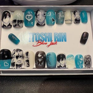 May include: A collection of press-on nails in a white box. The nails display diverse designs, such as anime-style character portraits, hearts, butterflies, and abstract patterns. The colour scheme includes teal, black, white, and grey. The text "TOSHI RIN Blue Jack" is visible.