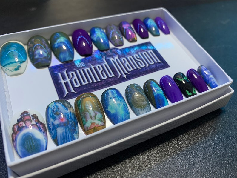 May include: A set of 18 coffin-shaped press-on nails with a Haunted Mansion theme. The nails feature images of ghosts, the Haunted Mansion sign, and other details from the Disney attraction. The nails are in a white box with the words "The Haunted Mansion" printed on the lid.