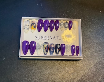 May include: A set of 12 purple and white press-on nails with various Supernatural themed designs. The designs include the show's logo, characters, and quotes. The nails are in a white box with the word "Supernatural" printed on it.