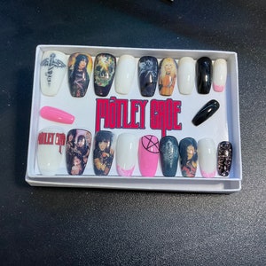 Op de afbeelding: Een set van 18 kunstnagels met verschillende ontwerpen met de band "Mötley Crüe". De ontwerpen omvatten bandleden, bandlogo's en pentagrammen. De nagels zitten in een witte doos met een roze en zwarte achtergrond.
