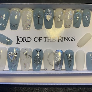 May include: A set of 14 blue and white false nails with Lord of the Rings themed designs. The designs include the One Ring, the Tree of Gondor, the Elvish symbol, and the symbol of the White Council.