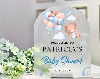 May include: A frosted acrylic welcome sign for a baby shower with a blue and brown color scheme. The sign features a teddy bear holding balloons, clouds, and stars. The text on the sign reads "Welcome to Patricia's Baby Shower 12.25.2027".