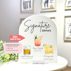 May include: White acrylic sign with a rounded top and the text "Signature Drinks" in black script. The sign features illustrations of four cocktails: a Pina Colada, an Old Fashioned, a Margarita, and a drink with a lime wedge. The sign also includes the text "550+ Drink Options" and "Customize with your: 1. Signature drinks 2. Sign Size 3. Acrylic/text color".