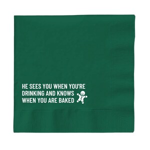 Op de afbeelding: Groene papieren servet met witte tekst die luidt "Hij ziet je wanneer je drinkt en weet wanneer je gebakken bent" en een afbeelding van een peperkoekman.