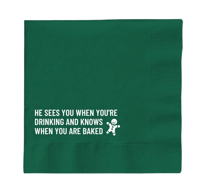 Op de afbeelding: Groene papieren servet met witte tekst die luidt "Hij ziet je wanneer je drinkt en weet wanneer je gebakken bent" en een afbeelding van een peperkoekman.