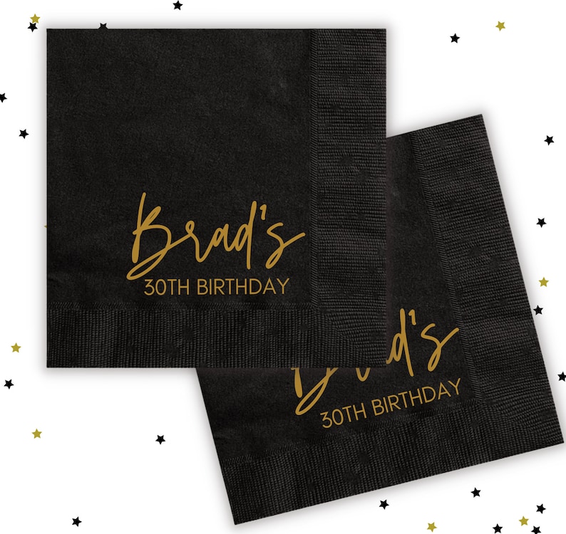 Puede incluir: Dos servilletas de papel negras con letras doradas. El texto en las servilletas dice "Brad's 30th Birthday".
