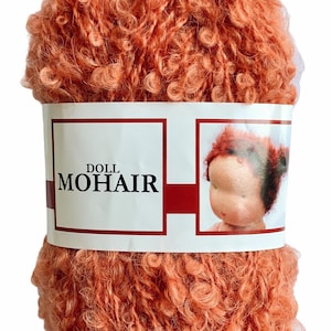 May include: A ball of peach-colored doll mohair yarn. The yarn is tightly curled and has a soft, fuzzy texture. A white label wrapped around the yarn reads "DOLL MOHAIR" with a doll's face on the right side.