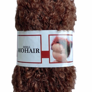 May include: A tightly wound ball of brown doll mohair yarn. The yarn is wrapped with a white label featuring the words "DOLL MOHAIR" and an illustration of a doll's face with red hair.