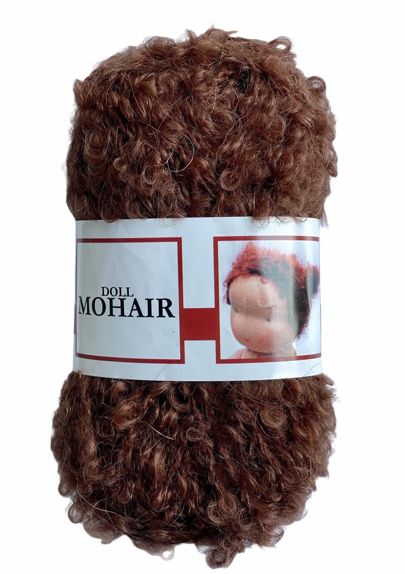 May include: A tightly wound ball of brown doll mohair yarn. The yarn is wrapped with a white label featuring the words "DOLL MOHAIR" and an illustration of a doll's face with red hair.