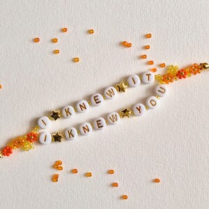 Puede incluir: Dos pulseras de cuentas con cuentas redondas blancas y letras doradas que forman las frases I KNEW IT e I KNEW YOU. Las pulseras incluyen peque&ntilde;as cuentas doradas en forma de estrella y cuentas de flores naranjas y amarillas, con cuentas sueltas.