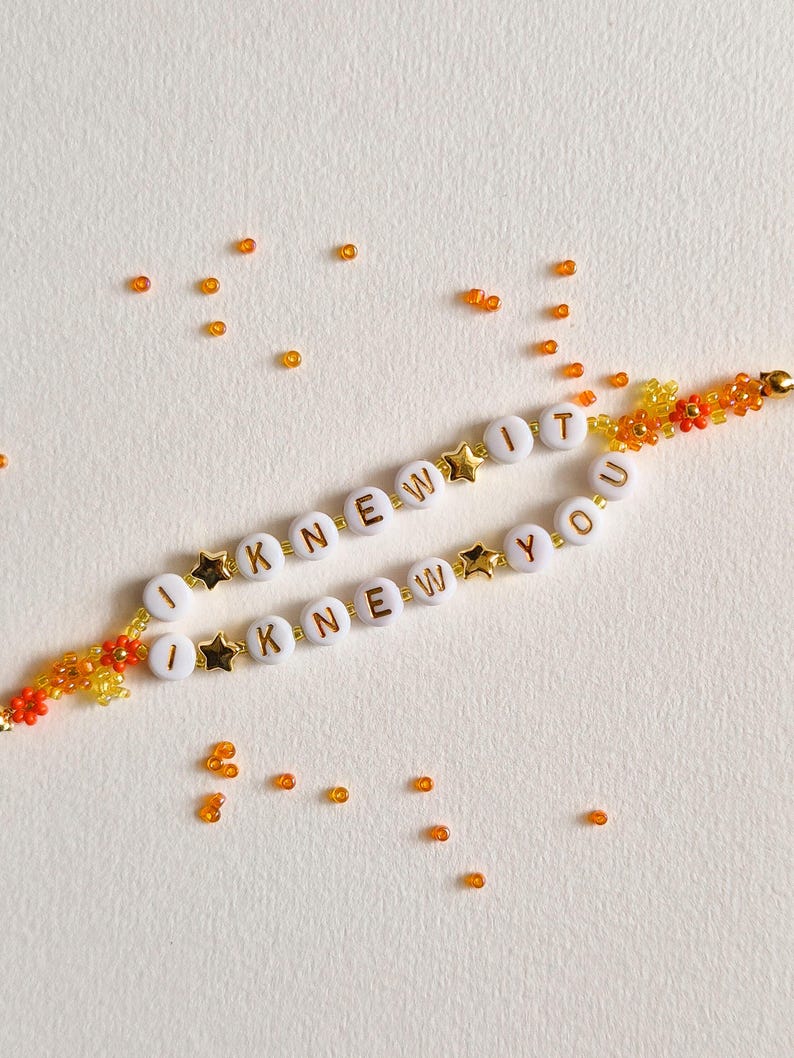 Puede incluir: Dos pulseras de cuentas con cuentas redondas blancas y letras doradas que forman las frases I KNEW IT e I KNEW YOU. Las pulseras incluyen peque&ntilde;as cuentas doradas en forma de estrella y cuentas de flores naranjas y amarillas, con cuentas sueltas.