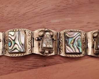 May include: A link bracelet featuring alternating rectangular panels of iridescent abalone shell and trapezoidal metal settings with decorative silver-toned metalwork, including beaded edges and scroll patterns, secured with a metal clasp.