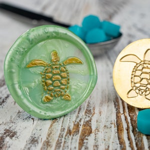May include: Two wax seals with a turtle design. One seal is green with a gold turtle, the other is gold with a gold turtle.