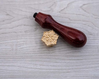 May include: A wooden handle wax seal stamp with a gold-colored snowflake design.
