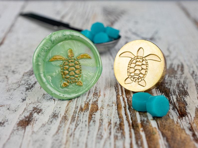 May include: Two wax seals with a sea turtle design. One seal is green with a gold turtle, the other is gold with a gold turtle.