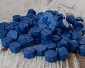 May include: A pile of blue wax seals, some with a hexagonal shape, and one with the initials "MK" embossed in the center.