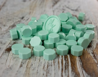 May include: A pile of light green wax seals, some are hexagonal shaped and some are round. One round seal has the letters "MBK" embossed on it.