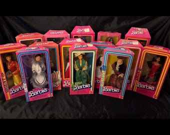 May include: A collection of eleven Barbie dolls in their original rectangular pink and yellow packaging. Each box features a clear plastic window displaying a doll dressed in various international cultural outfits, with labels like Orient, Arctic, Irish, and Spain.