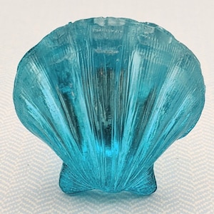 May include: A light blue seashell shaped decorative object. The seashell is made of glass and has a textured surface.