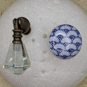 May include: A clear glass knob with a brass base and a blue and white ceramic knob with a fan pattern.