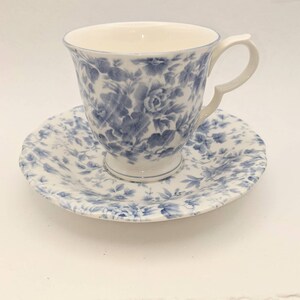 May include: A white teacup and saucer with a blue floral pattern. The cup has a handle and the saucer has a scalloped edge.