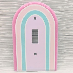 May include: A light pink, light blue, and white rainbow light switch cover.