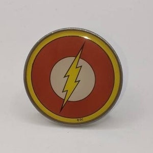 May include: A round pin with a yellow border and a red center. The center features a white circle with a yellow lightning bolt inside.