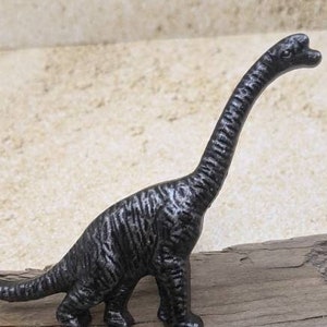 May include: A black cast iron dinosaur figurine. The dinosaur is standing on a piece of weathered wood.