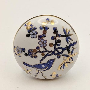 May include: A white ceramic knob with a blue and gold floral design featuring a bird. The knob has a glossy finish.