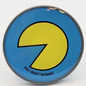 May include: A round blue and yellow Pac-Man pin with the text "PAC-MAN TM & ©BNEI" on the bottom.
