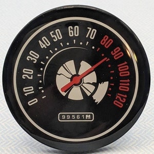 May include: A black round gauge with a white face and red needle. The gauge has white numbers from 0 to 120 and the text "99561M".