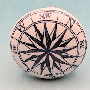 May include: White ceramic knob with a black compass rose design. The compass rose features the cardinal directions: N, S, E, W, NE, NW, SE, SW.