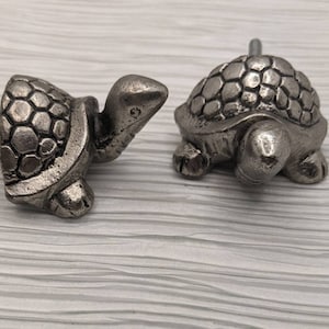 May include: Two silver turtle shaped drawer pulls. The turtles are facing different directions.