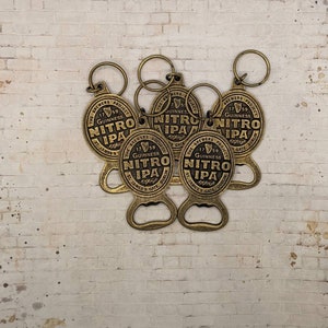 May include: Five gold-colored bottle openers with key rings. Each opener has a round, embossed design with the text "The Brewers Project 1759 Guinness Nitro IPA St. James's Gate Dublin".