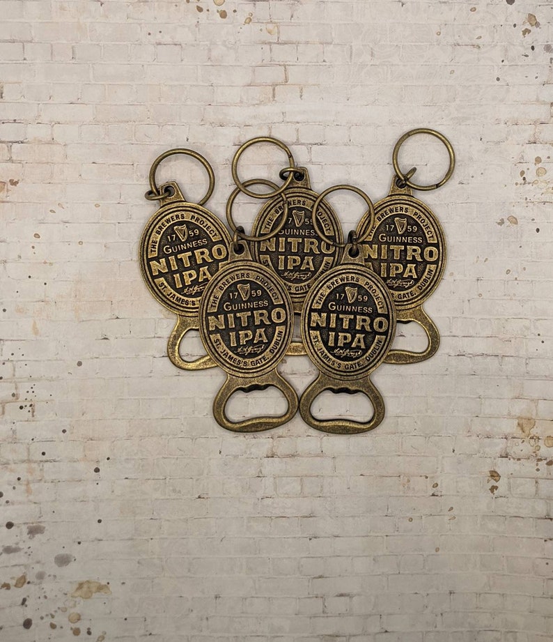 May include: Five gold-colored bottle openers with key rings. Each opener has a round, embossed design with the text "The Brewers Project 1759 Guinness Nitro IPA St. James's Gate Dublin".