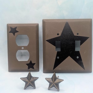 May include: A set of brown electrical outlet and switch covers with black star designs. Two star-shaped knobs are also included. The outlet cover has two openings and two small stars. The switch cover has two switch openings and a large star.