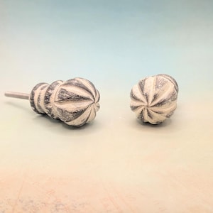 May include: Two white and gray decorative cabinet knobs with a textured, fluted design. The knobs have a metal screw for attaching to a cabinet door.