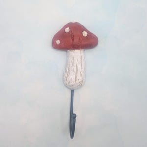 May include: A decorative mushroom-shaped wall hook. The mushroom cap is a deep red with white spots, and the stem is white with a textured finish. The hook itself is black. This whimsical hook is perfect for a child's room or a nature-themed space.